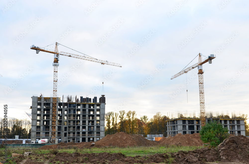 Tower cranes working at construction site against blue sky. Crane lifting a concrete bucket. Construction process of the new residential buildings. Transportation blocks and pouring of the cement mix