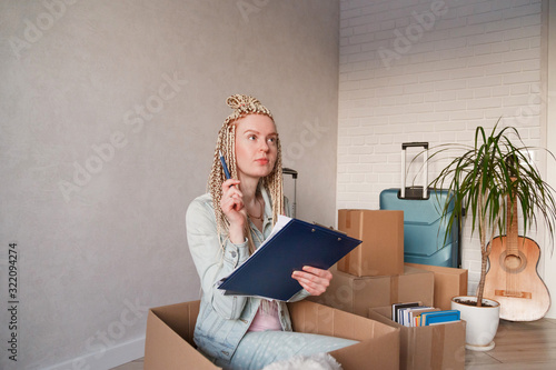 Beautiful woman sitting in box in casual clothes is packing her stuff into the boxes, making notes photo