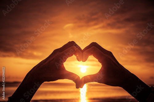 Handgeformtes Herz bei Sonnenuntergang am Meer
