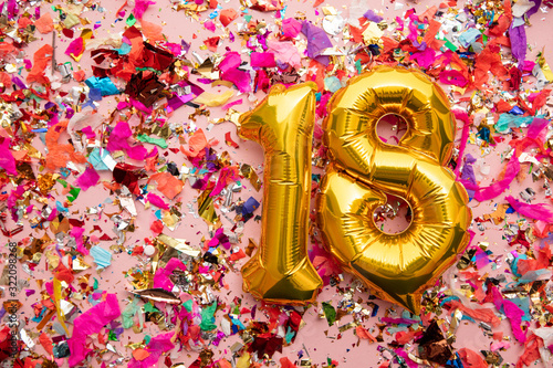 Number 18 gold birthday celebration balloon on a confetti glitter background