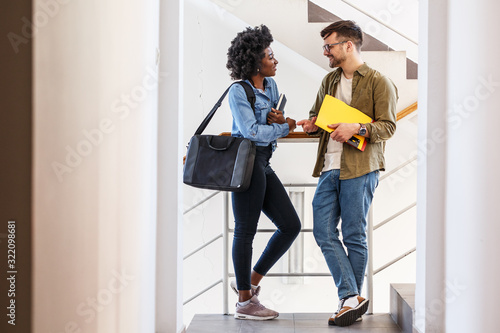 In the college lobby, a female and a male student engage in a lively conversation before their lecture, sharing insights and building connections in the vibrant atmosphere of learning.