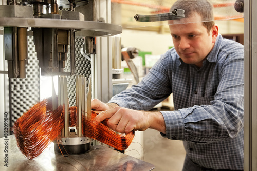Foto Skilled worker at a robot machine that winds coils for an electric motor