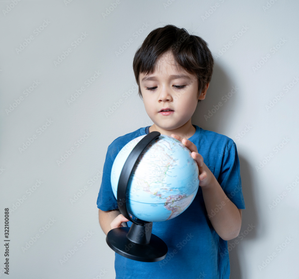 Portrait child boy standing next to the wall looking a globe with curious face, Selective focus School kid Child boy learning about Geography, Education and Homeschooling Portrait child boy standing next to the wall looking a globe with curious face, Selective focus School kid Child boy learning about Geography, Education and Homeschooling