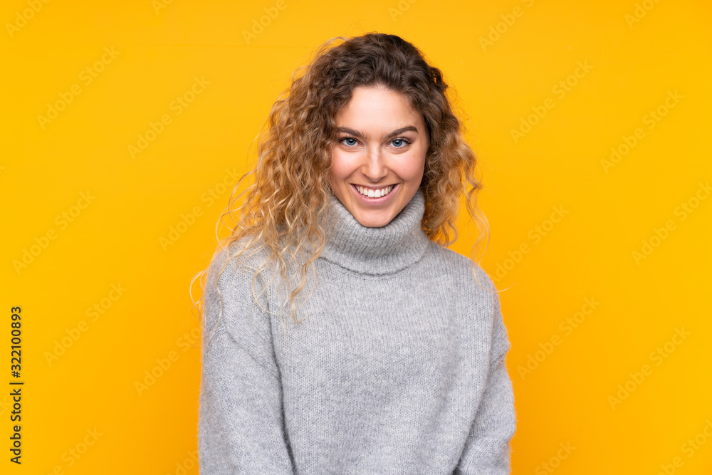 Young blonde woman with curly hair wearing a turtleneck sweater isolated on yellow background laughing Young blonde woman with curly hair wearing a turtleneck sweater isolated on yellow background laughing