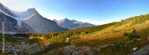 Panorama of Mount Edith Cavell. High mountains with glacier, sun rays illuminate the forest. Sunny day, blue sky, Canadian Rockies. 