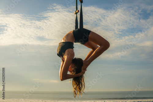 Schilderij op canvas aero yoga beach workout - young attractive and athletic woman practicing aerial