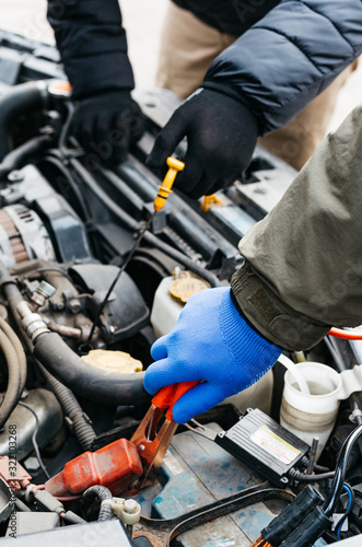 Two Car mechanic engineers checking, fixing the car, making maintenance comprehensive auto check. Auto mechanic charging car battery with electricity using jumper cables. Car repair service