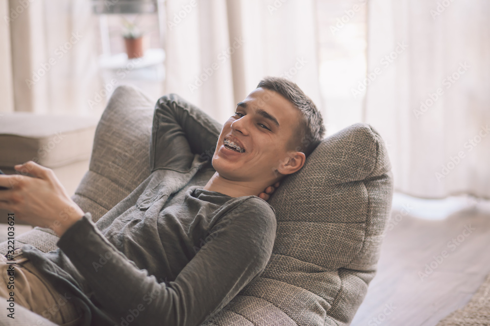 Handsome teenage guy relaxing on modern soft couch at home in living room Handsome teenage guy relaxing on modern soft couch at home in living room