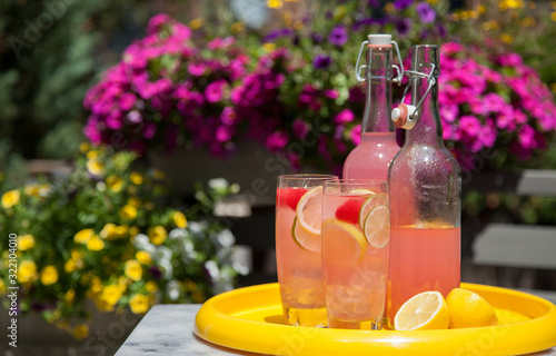 Glasses of pink lemonade with lemons, limes, and raspberries on a tray in the sunshine