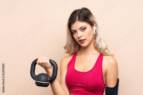 Teenager sport girl over isolated background making weightlifting with kettlebell