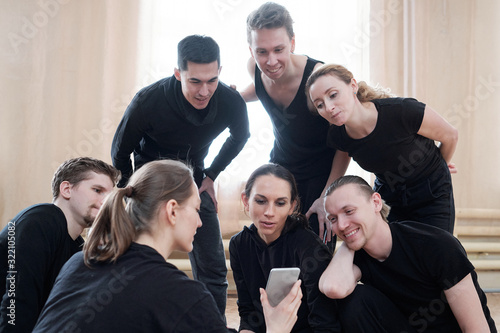 Group of young male and female dancers wearing black clothes spending time together watching something on smartphone © pressmaster