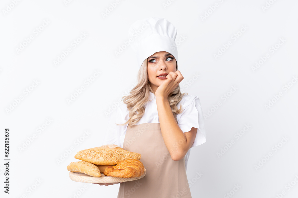 Teenager girl in chef uniform. Female baker holding a table with several breads over isolated white background nervous and scared Teenager girl in chef uniform. Female baker holding a table with several breads over isolated white background nervous and scared