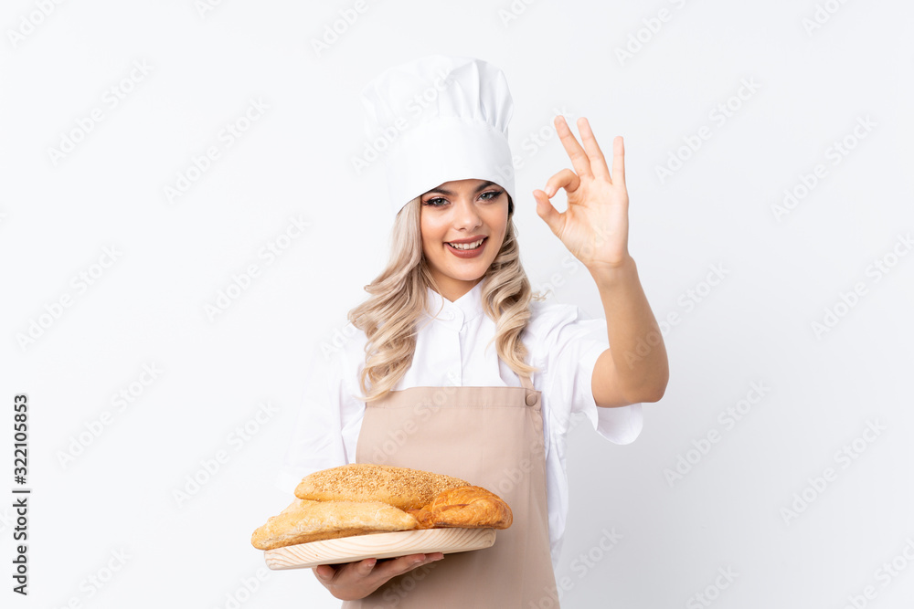 Teenager girl in chef uniform. Female baker holding a table with several breads over isolated white background showing an ok sign with fingers