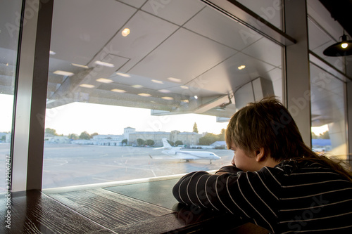 Boy at the airport waiting and looking at the departing planes from a window. Selective focus