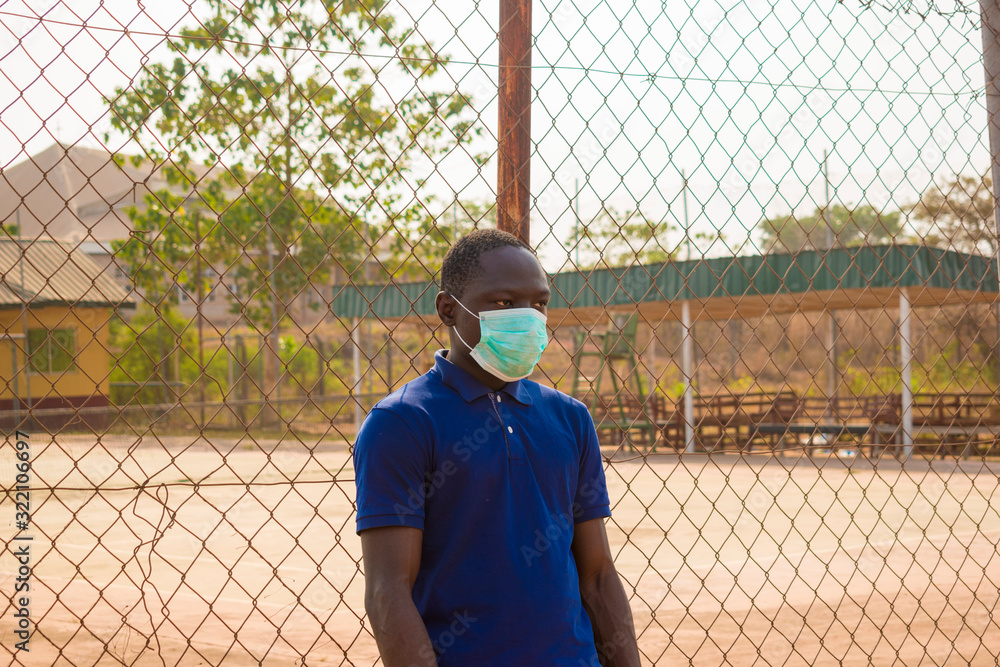 young black man standing alone outside wearing a medical face mask