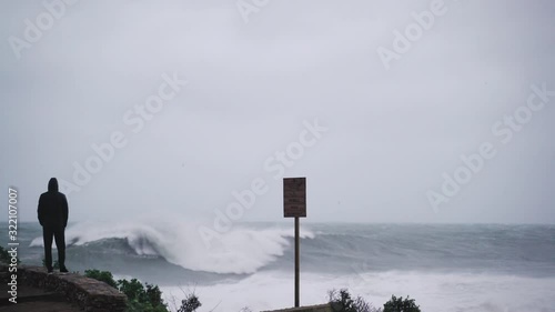 The man looks at the raging sea. A man is watching the storm. Silhouette of a man. Severe stormy sea. Big waves. Windy rainy weather. View of the dramatic ocean. The wind is blowing.