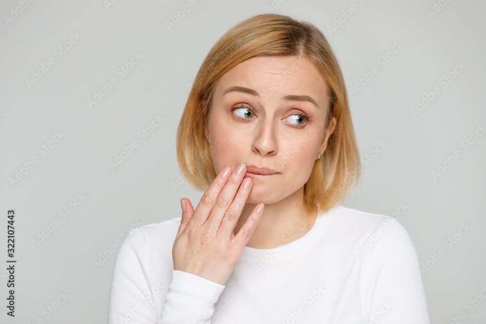 Oops, how awkward! Close up portrait of shy awkward young woman biting lips feeling embarrassed, confused and nervous, looking aside, covers mouth with her hand. Isolated on grey background. Oops, how awkward! Close up portrait of shy awkward young woman biting lips feeling embarrassed, confused and nervous, looking aside, covers mouth with her hand. Isolated on grey background.