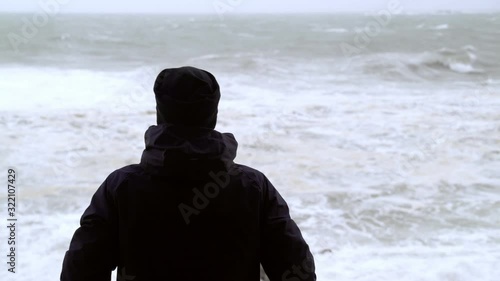 The man looks at the raging sea. A man is watching the storm. Silhouette of a man. Severe stormy sea. Big waves. Windy rainy weather. View of the dramatic ocean. The wind is blowing.