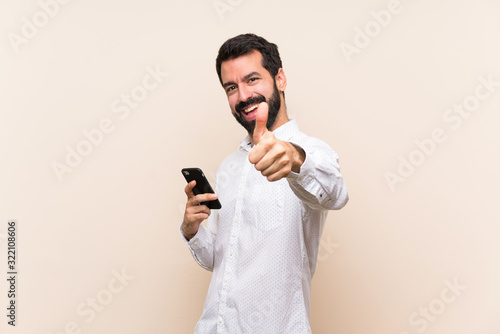 Young man with beard holding a mobile with thumbs up because something good has happened