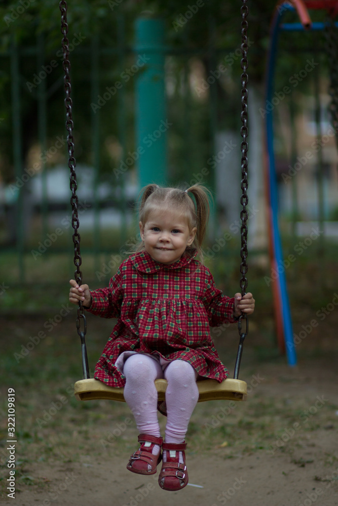 Happy caucasian child of two years old sitting on chain swing and swinging looking at camera Happy caucasian child of two years old sitting on chain swing and swinging looking at camera
