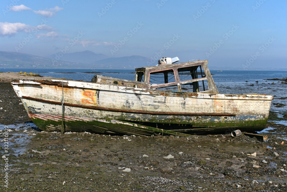 Wooden boat wreck in a bay with blue sky, some clouds and mountains in the background