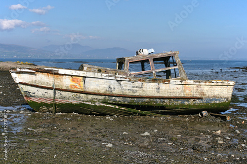 Wooden boat wreck in a bay with blue sky, some clouds and mountains in the background