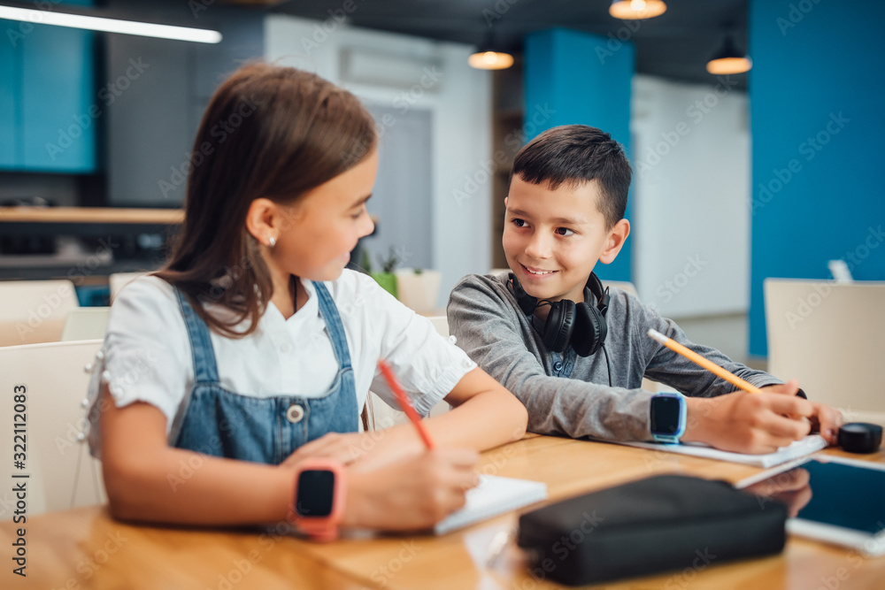 Two small friends writing homework at modern blue classroom. Two small friends writing homework at modern blue classroom.