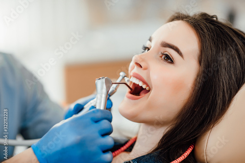 Cropped image. Happy young woman lying with opened mouth. Male dentist in gloves using restoration instruments.