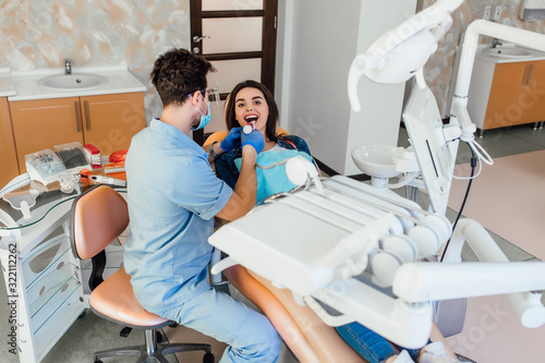 The woman came to visit the dentist. She sits in the dental chair. The dentist bent over her. Happy patient and dentist concept.