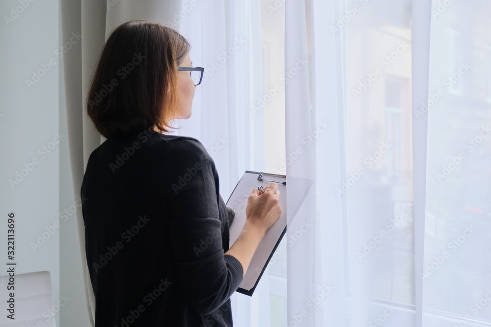 Mature woman couch taking notes standing near window in office Mature woman couch taking notes standing near window in office