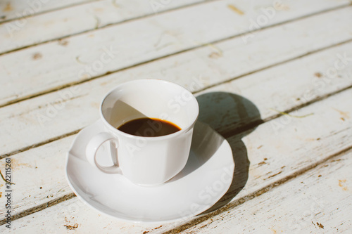 Cup of coffee on white wooden background with warm sunlight in the morning.
