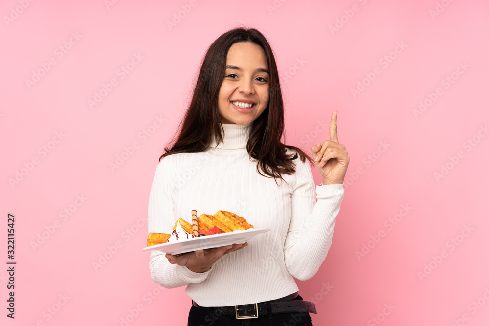 Young brunette woman holding waffles over isolated pink background pointing up a great idea Young brunette woman holding waffles over isolated pink background pointing up a great idea