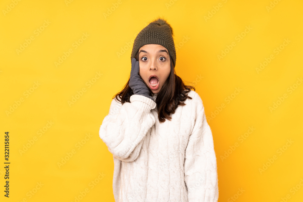 Young woman with winter hat over isolated yellow background with surprise and shocked facial expression Young woman with winter hat over isolated yellow background with surprise and shocked facial expression