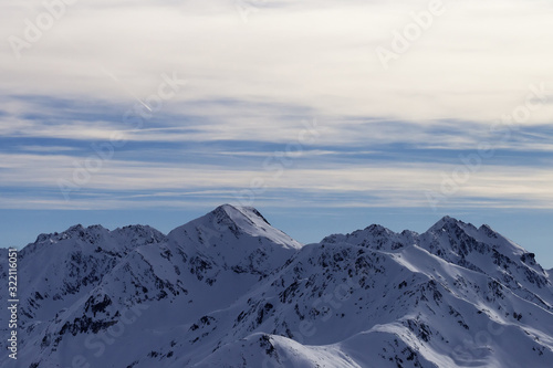 Snowy high mountains and sunlit cloudy sky at winter evening