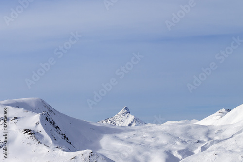 High mountains with snowy peak and sunlit cloudy sky at winter