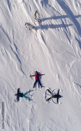 a group of young people in bright ski suits depict snow angels lying on the fresh snow in the form of a cross. four winter angels happy and energetic. Winter fun at the ski resort photo