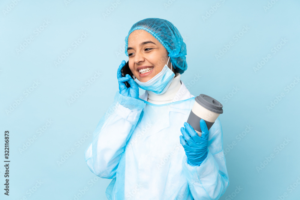 Young surgeon Indian woman in blue uniform holding coffee to take away and a mobile Young surgeon Indian woman in blue uniform holding coffee to take away and a mobile
