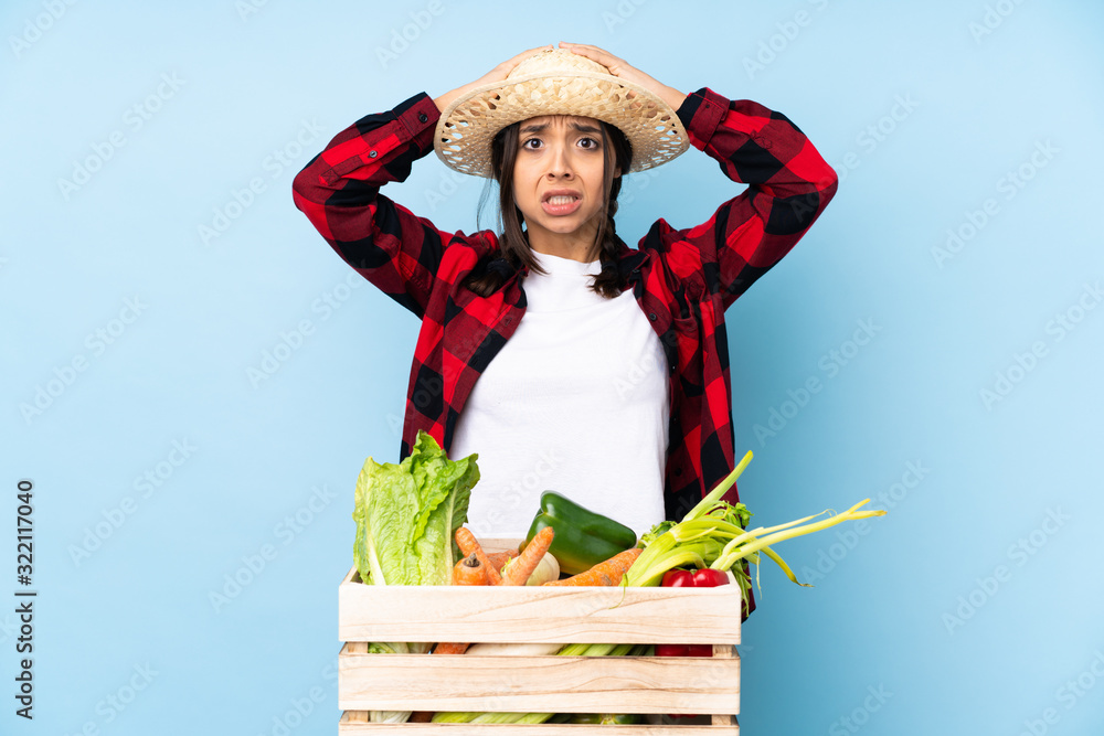 Young farmer Woman holding fresh vegetables in a wooden basket frustrated and takes hands on head