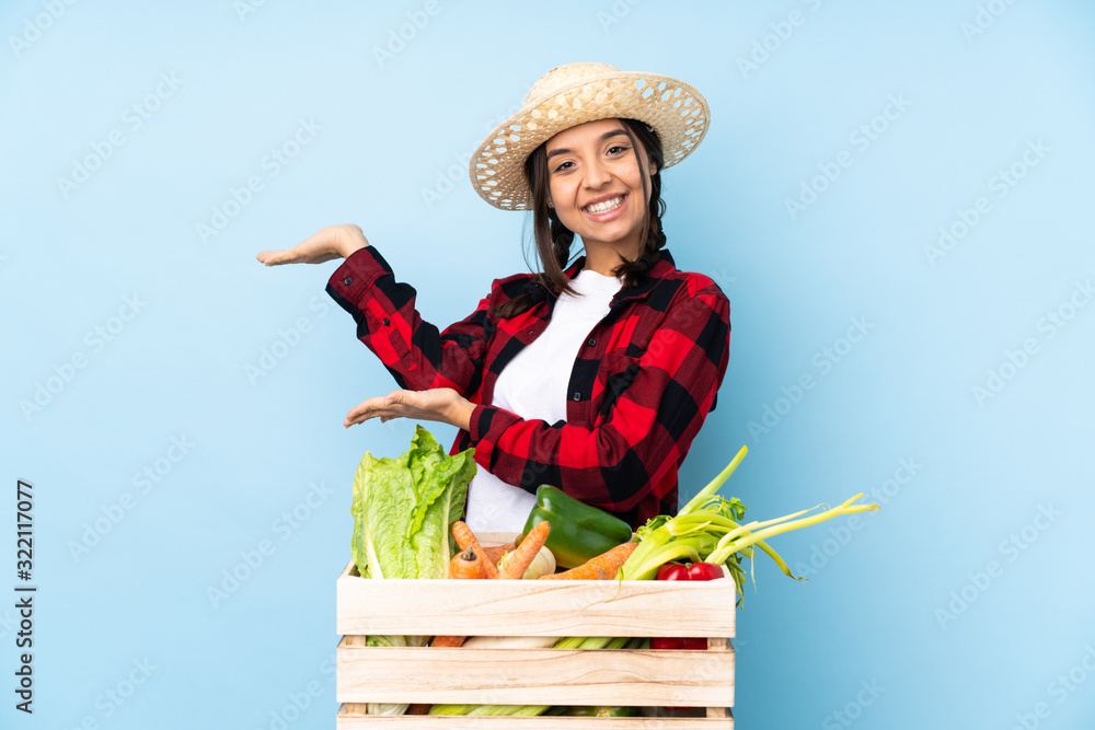 Young farmer Woman holding fresh vegetables in a wooden basket extending hands to the side for inviting to come