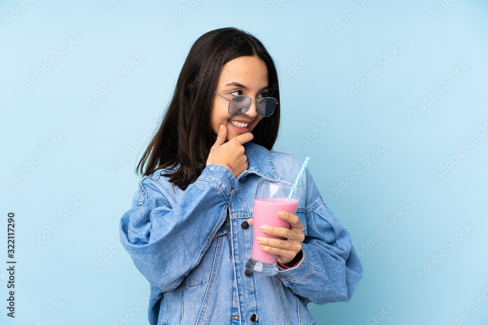 Young woman with strawberry milkshake over isolated blue background looking to the side Young woman with strawberry milkshake over isolated blue background looking to the side