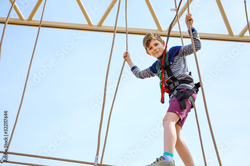 Happy little kid boy climbing on high rope course trail. Active child making adventure and action on family vacations. Challenge for brave kids.