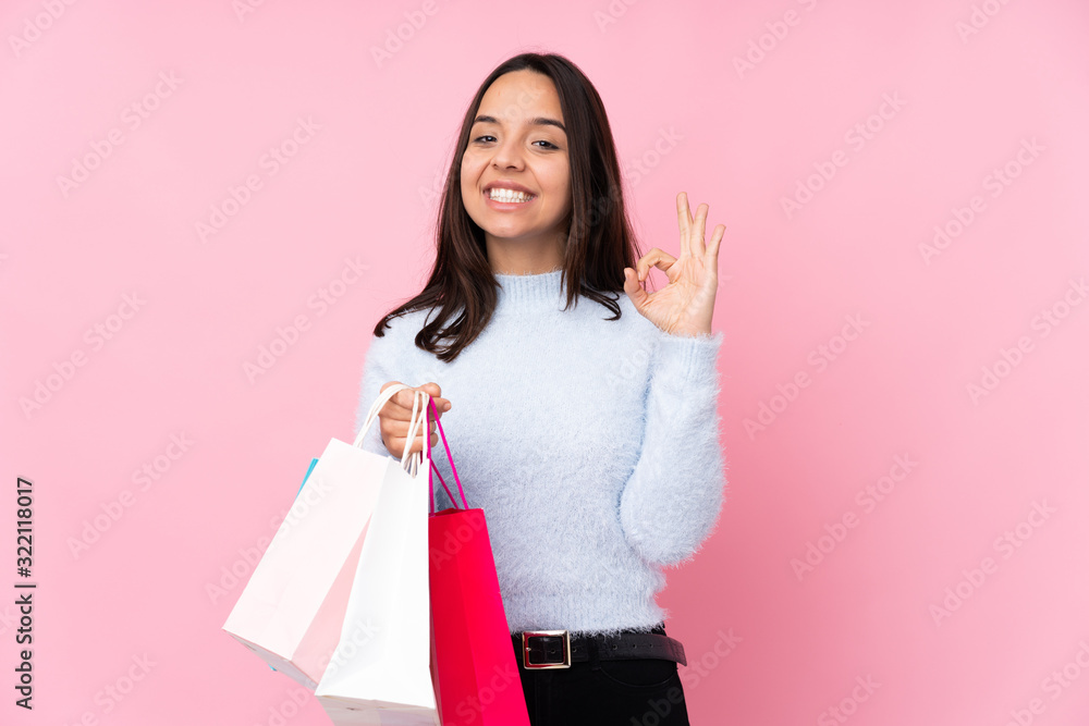Young woman with shopping bag over isolated pink background showing ok sign with fingers