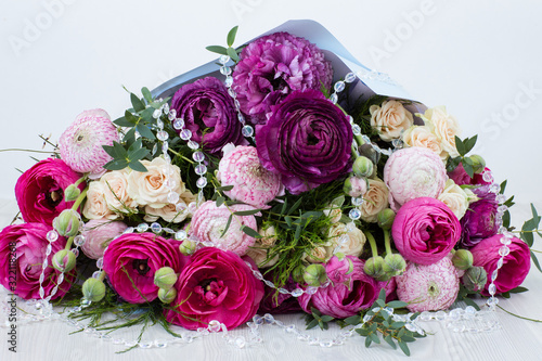 on a light background a bouquet of ranunculus and roses and transparent beads