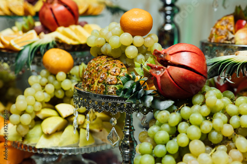 Fototapeta Naklejka Na Ścianę i Meble -  Fruits on wedding table at restaurant. Composition of colored fruit, close-up. Decoration with fruit for child birthday. Sweet table with fruit, wedding catering, fruit bar on party