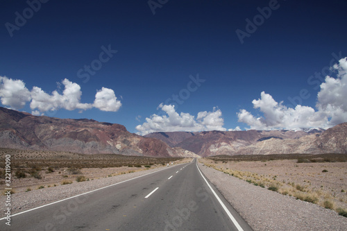 długa płaska droga asfaltowa ciągnąca sie po horyzont z górami i niebem w tle