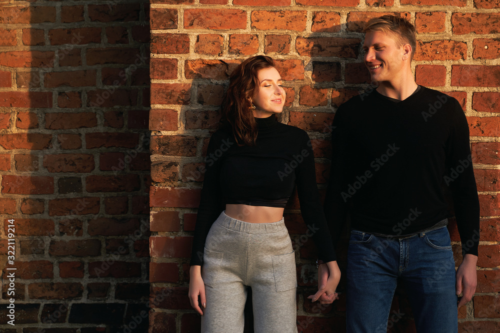 Romantic couple young beautiful sensual redhead woman and tall handsome blonde man posing in sunset sunlight on red brick wall background