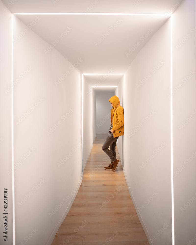 Chico con abrigo amarillo en pasillo futurista con luces apoyado sobre la pared