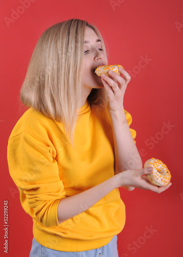 Smiling caucasian woman with pink donuts posing on red background in studio.