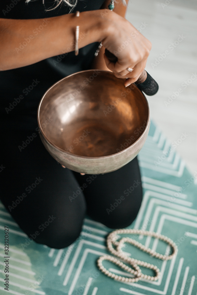 Close up image of woman’s hands holding Tibetan Singing Bowl indoors. The atmosphere of relaxation and Zen. Exercise for achieving clarity of mind and perfect body.
