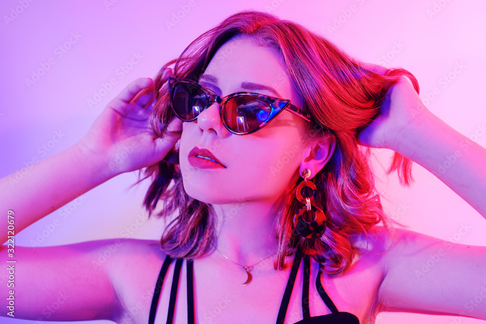 Beautiful girl in neon. Fashion photo of a short-haired girl, dancing, sun glasses. Girl in red and blue light posing.